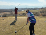 Man standing with his hands on his head wearing a red polo and tan pants. Man wearing a striped polo holding a golf driver 