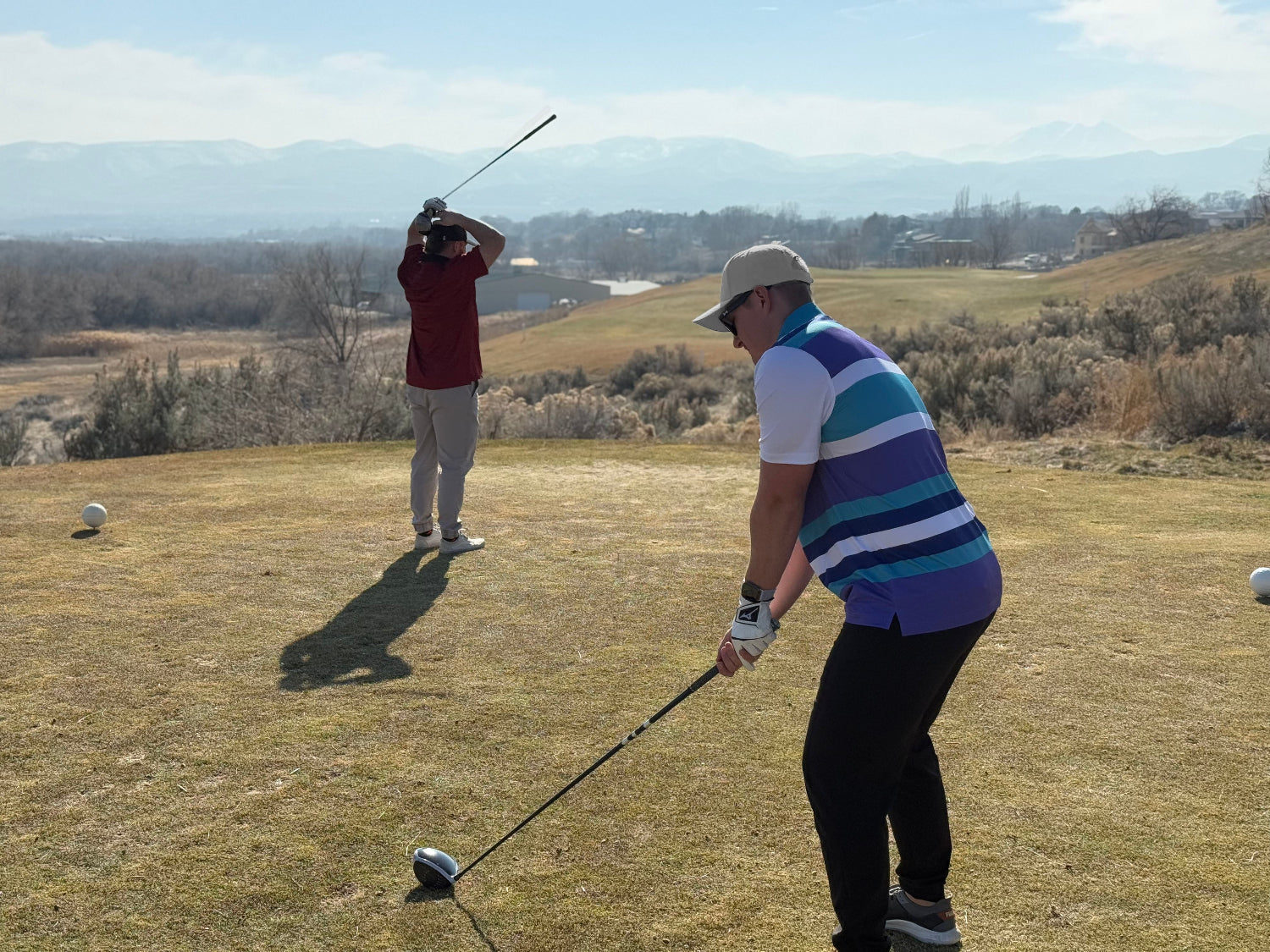 Man standing with his hands on his head wearing a red polo and tan pants. Man wearing a striped polo holding a golf driver 