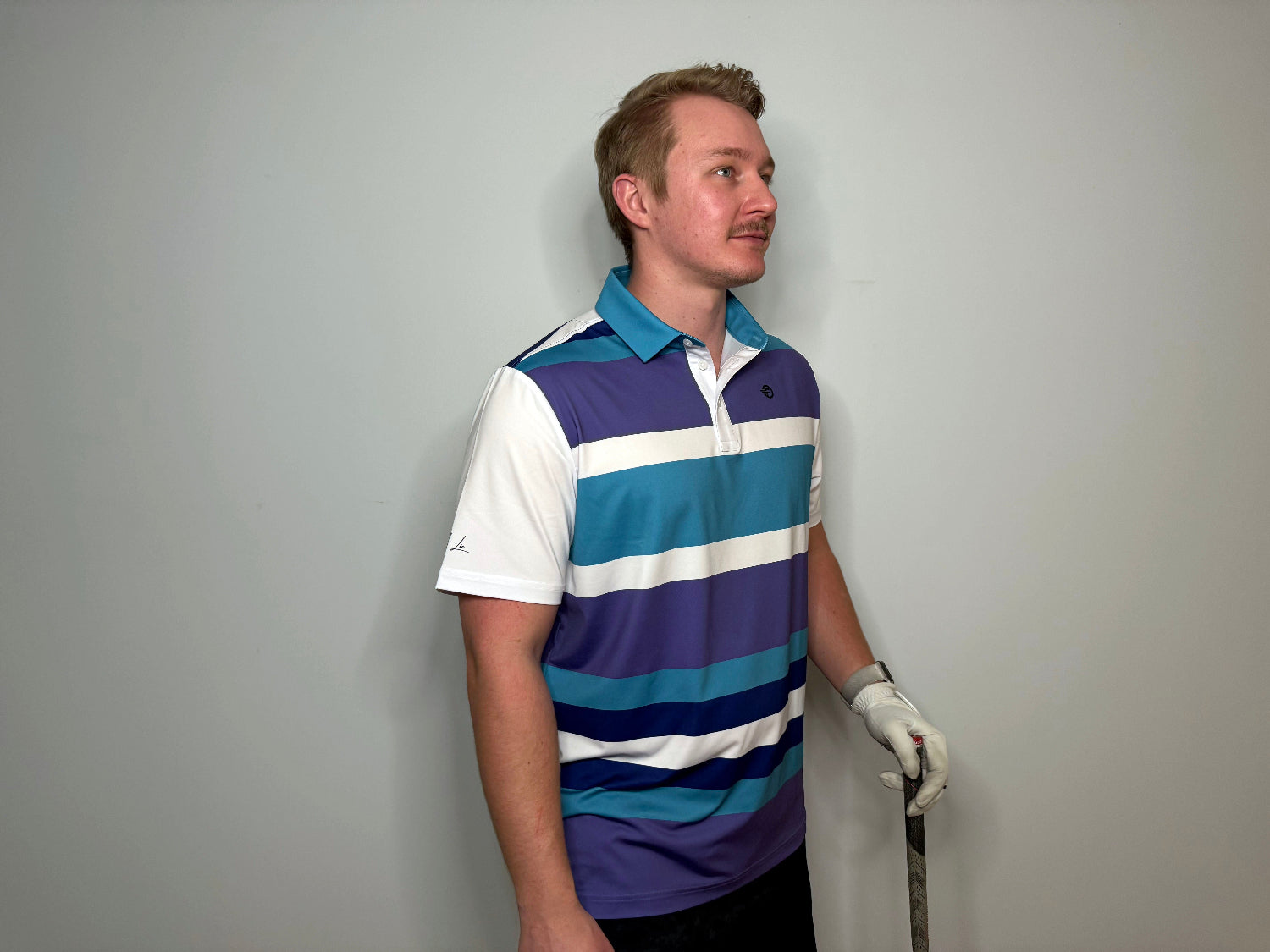 Man Wearing a polo with purple white teal and blue strips and a golf iron in his hand