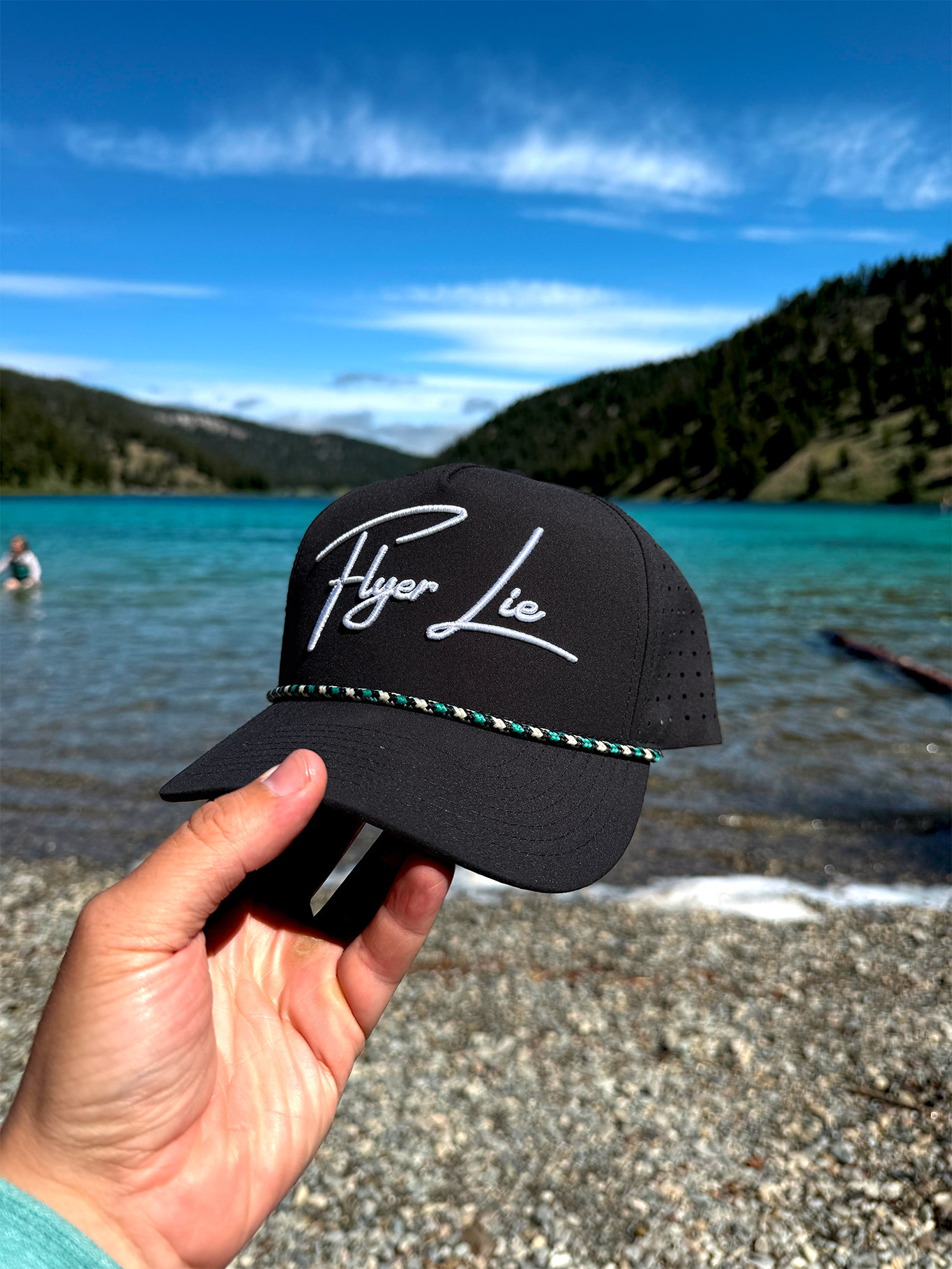 Black ball cap being held by hand in front of lake 