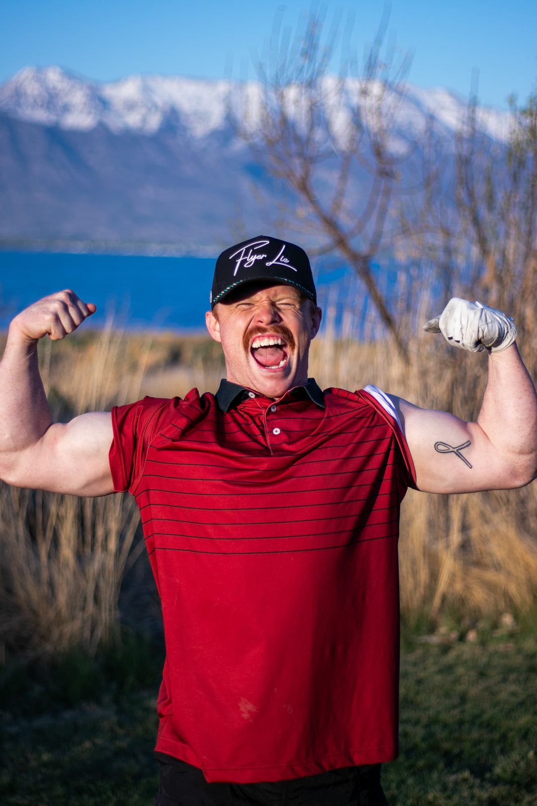 Man flexing muscles outdoors with mountains and lake in the background