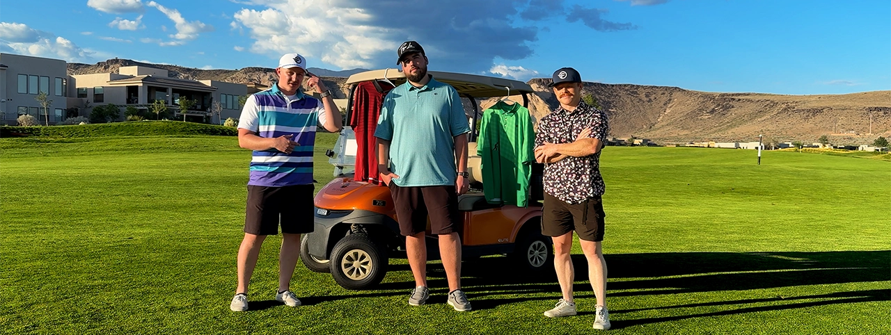 Three men standing next to a golf cart on a golf course with a clear sky.