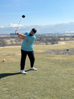 A person playing golf, mid-swing, wearing a blue polo shirt.