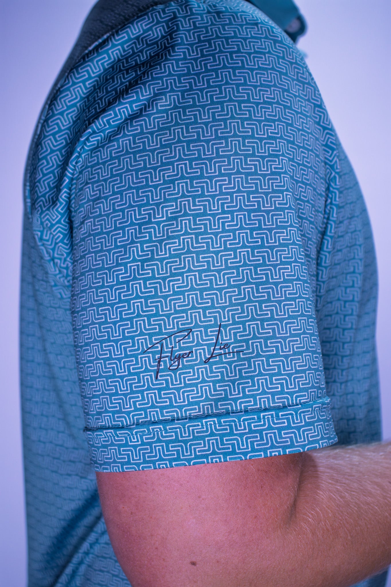 Close-up of a person wearing a blue patterned shirt with a signature on a light purple background