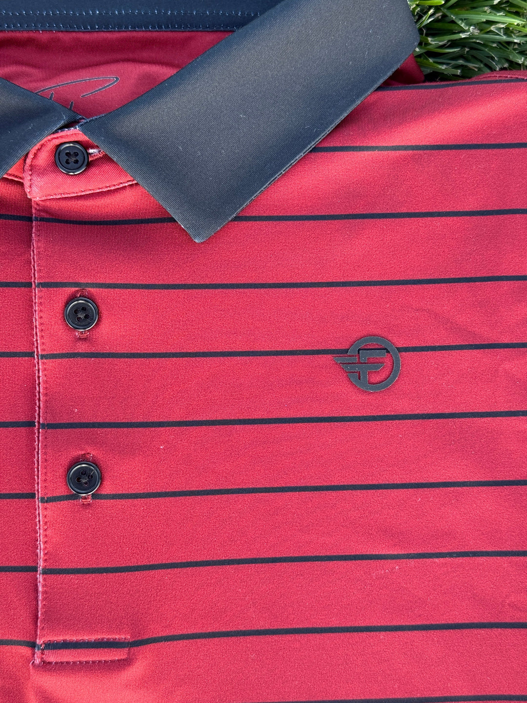Red polo with black horizontal stripes and a logo on a grassy background