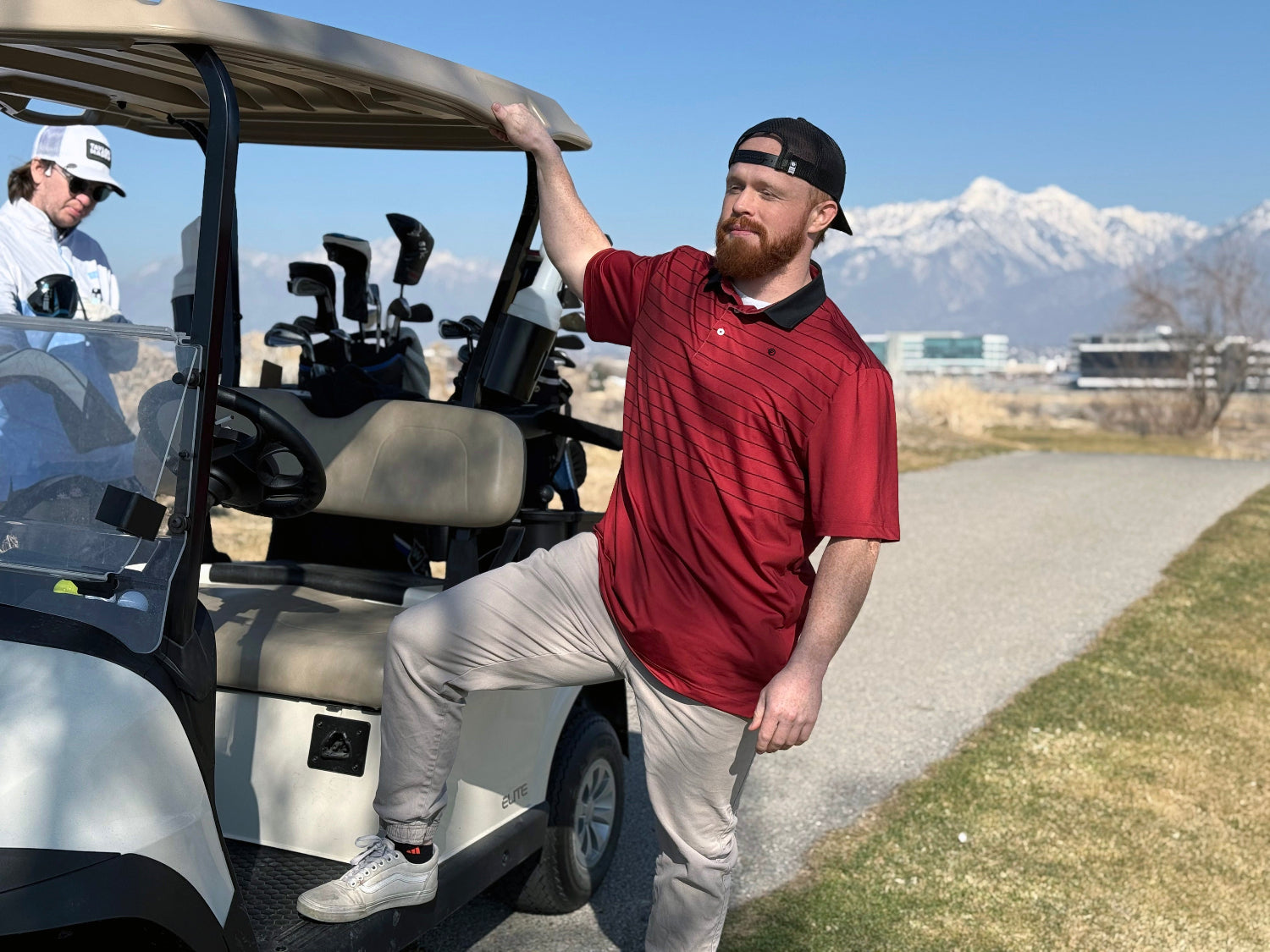 Man standing on the side of a golf cart wearing a red polo from flyer lie