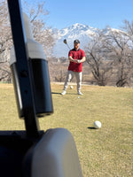 Man wearing a red polo with black horizontal stripes on the tee box. A mountain in the background 