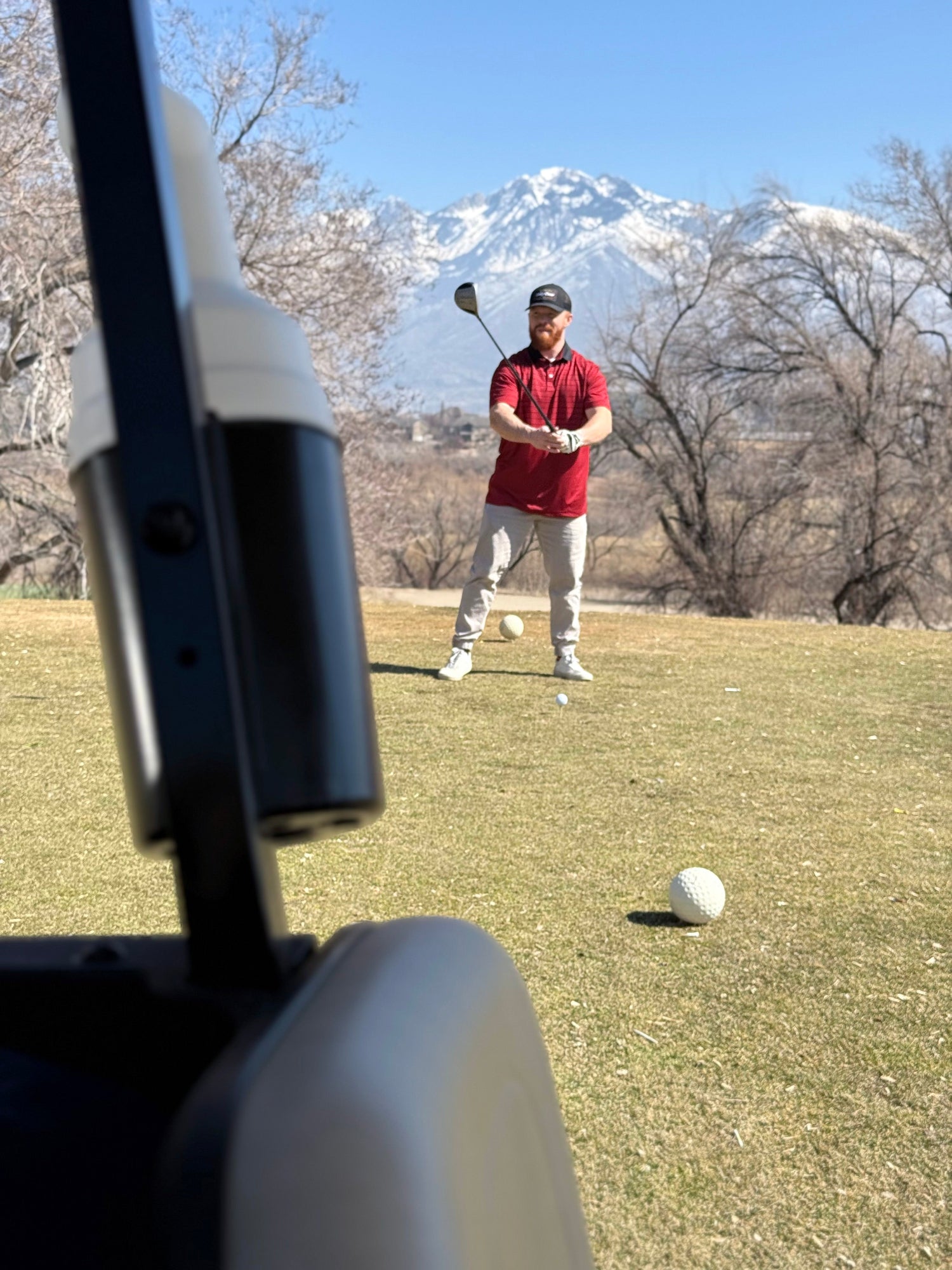 Man wearing a red polo with black horizontal stripes on the tee box. A mountain in the background 