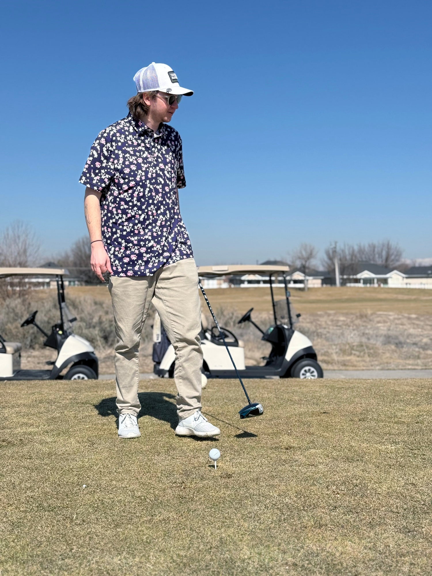 Man walking up to a golf ball placed on a tee on a tee box at riverbend golf course in Riverton Utah. Has a Taylormade Sim 2 driver in hand