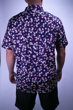 Person wearing a short-sleeve shirt with a floral pattern on a plain background