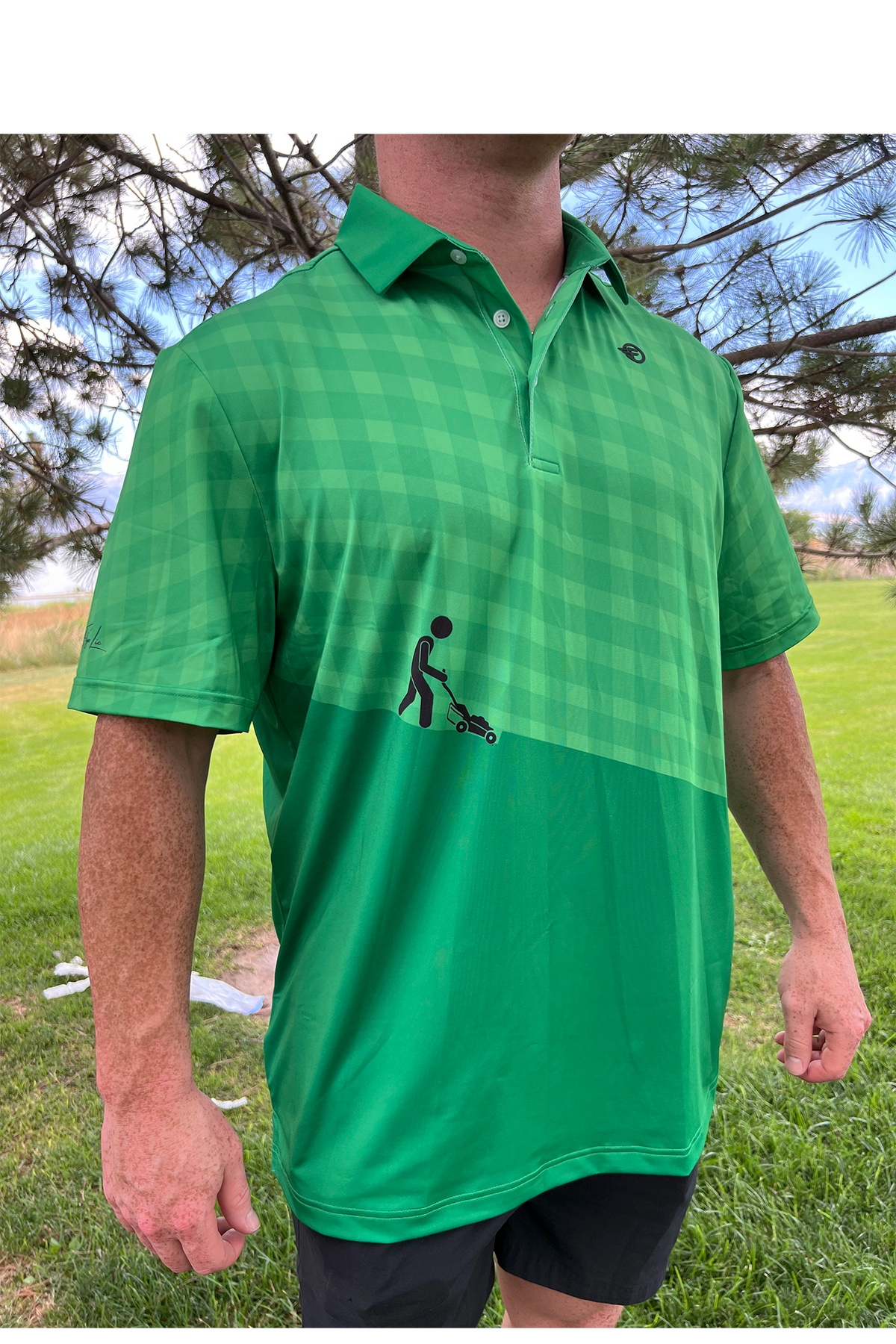 Person wearing a green checkered polo shirt with a graphic on a grassy background